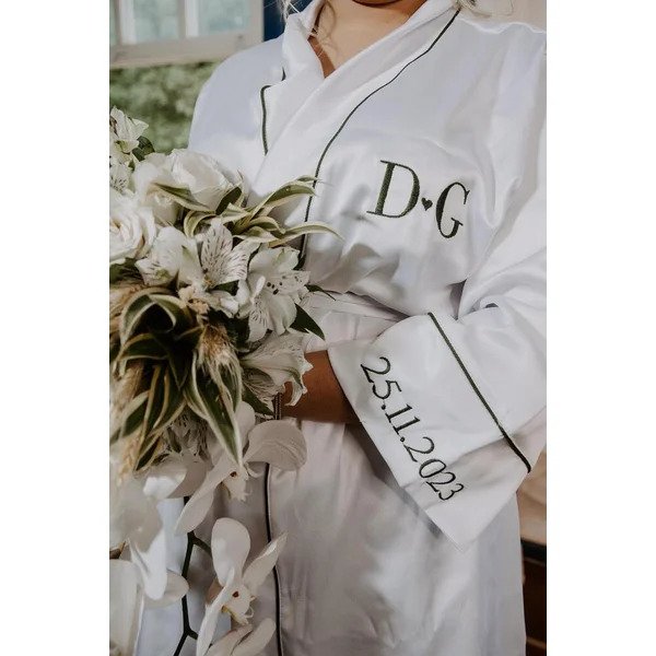 noiva segurando buque com robe com bordados em preto com data na manga e iniciais na altura do peito