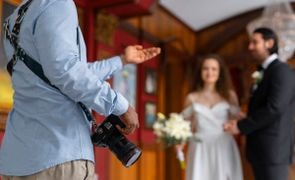 fotografo de vista lateral segurando camera com casal de noivos desfocad ao fundo