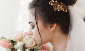 visao lateral de noiva com grinalda dourada veu branco e segurando buque