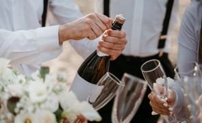 homem abrindo garrafa de espumante com pessoas com taca perto esperando 1