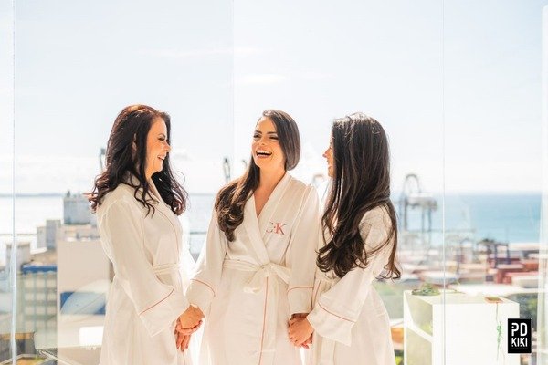 tres mulheres na sacada de dia com fundo desfocad usando robe branco com bordados em rosa
