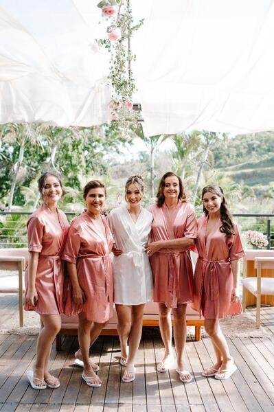 noiva com robe branco e madrinhas com robe rosa com plantas ao fundo
