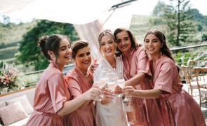 noiva com robe branco no centro e madrinhas com robe rosa todas segurando uma taca de champanhe