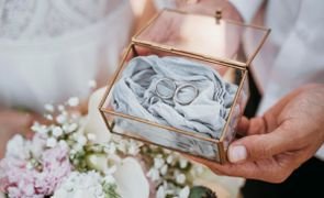 noivo ao lado da noiva segurando caixa de vidro com tecido e aliancas sobre