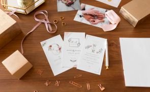 tres convites de casamento sobre mesa com clipes caixas fitas e fotos dos noivos ao redor