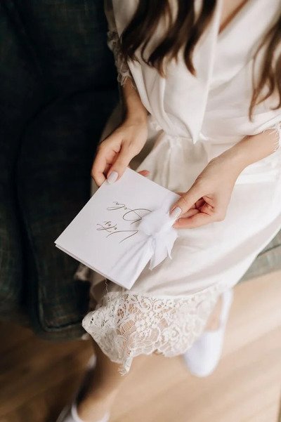 foto superior de noiva de robe segurando votos sobre pernas cruzadas