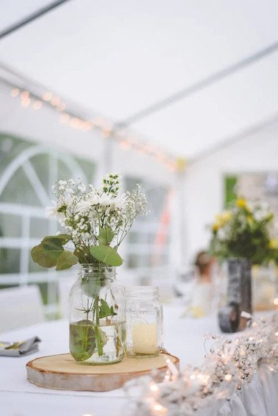 flores brancas em pote de vidro com agua e vela sobre madeira redonda sobre a mesa