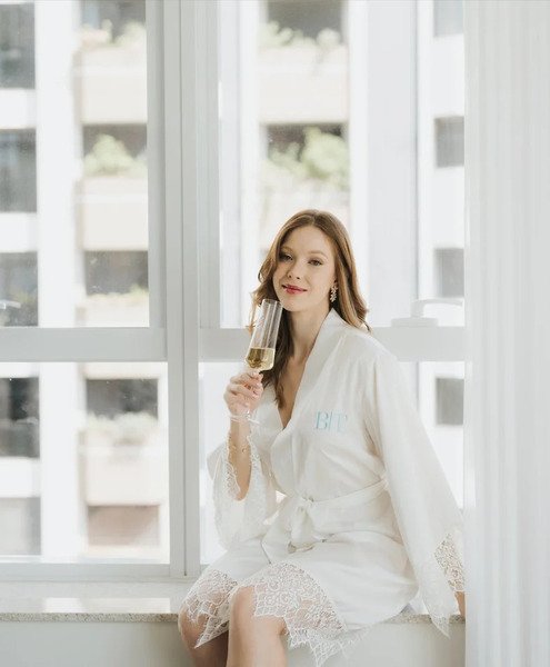 modelo sentada na janela com taca de champanhe usando robe personalizado com detalhes em renda curto robe adriely