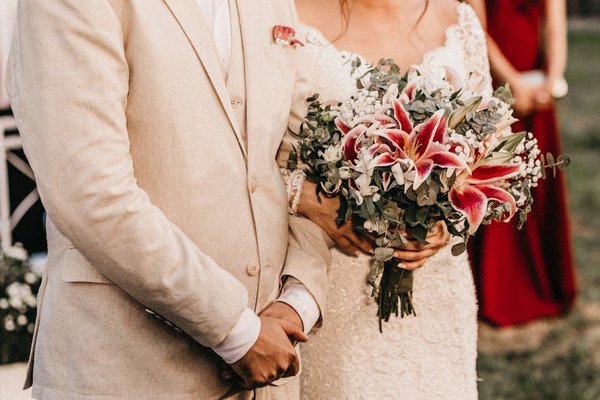 noivo e noia com bracos dados e noiva segurando buque de lirios rosas