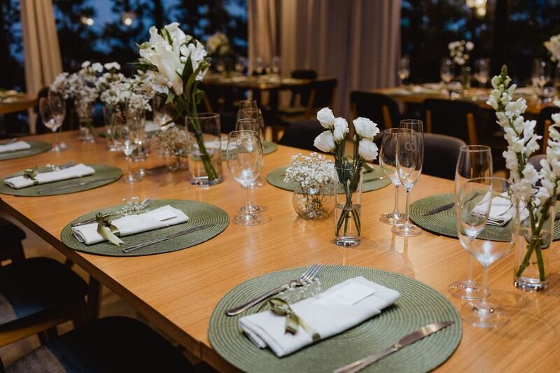 mesa com souplat verde talhares pratas sobre e guranapo no centro com vasos de vidros com flores branca sobre a mesa
