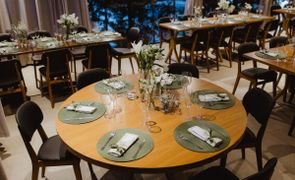 mesas redondas com sousplat verde e vasos de vidro com flores brancas