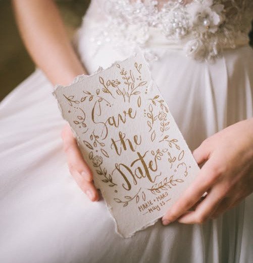 noiva segurando papel com escrito em dourado save the date data e nomes