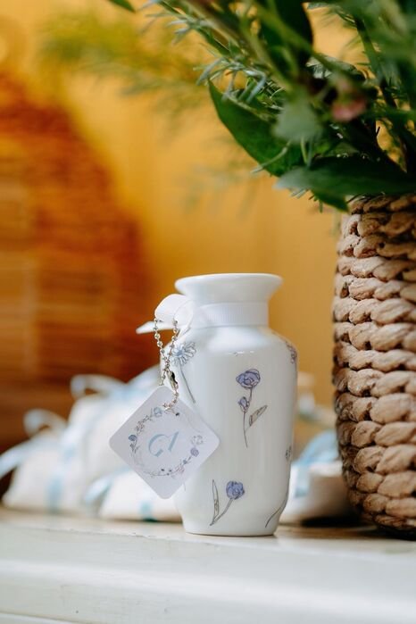 vaso bem pequeno com desenho de flores azuis e papel de iniciais dos noivos pendurado