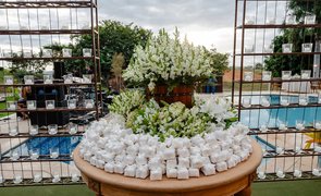 mesa redonda de madeira no gramado com bem casados brancos e flores brancas
