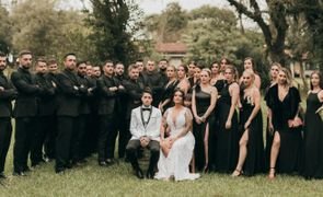 noivos de branco sentados no centro com madrinhas e padrinhos de preto de pe atras