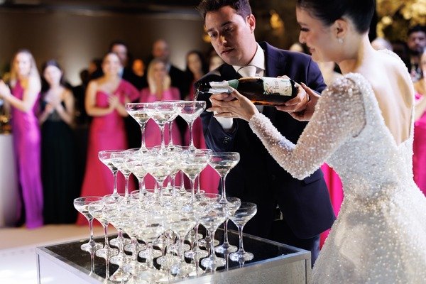 marido e eposa segurando a mesma garrafa de chamapnhe despejando em torrde de tacas