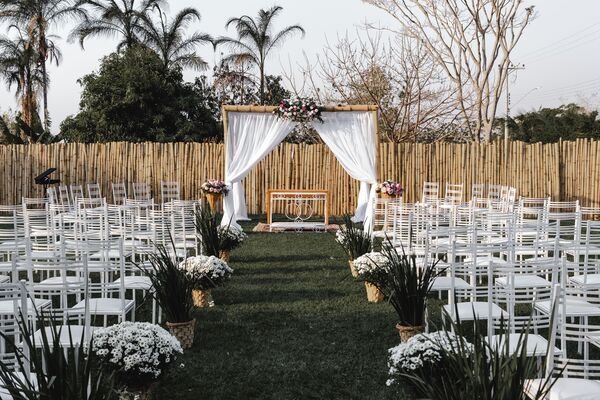 casamento organizado em ambiente externo cadeiras brancas no gramado e altar com cortina branca