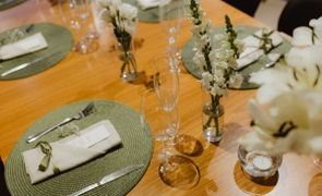 imagem superior de mesa posta com soupalt redondo verde talheres guardanapo e flores brancas em vasos de vidro