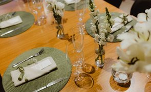 imagem superior de mesa posta com soupalt redondo verde talheres guardanapo e flores brancas em vasos de vidro