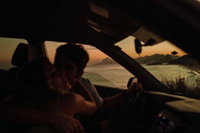 casal dentro do carro com noivo beijando a bochecha da noiva e mar ao fundo