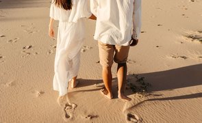 casal de costas noiva de branco e nivo de camisa branca e shorts bege caminhando na areia casal de costas noiva de branco e nivo de camisa branca e shorts bege caminhando na areia